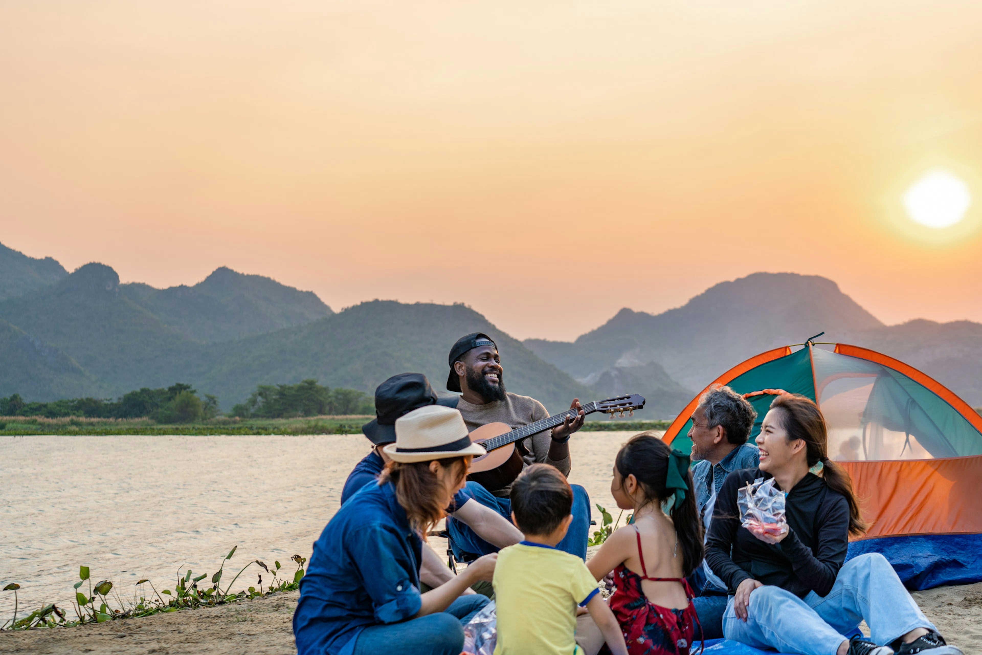 Image of a happy family camping by a lake playing music